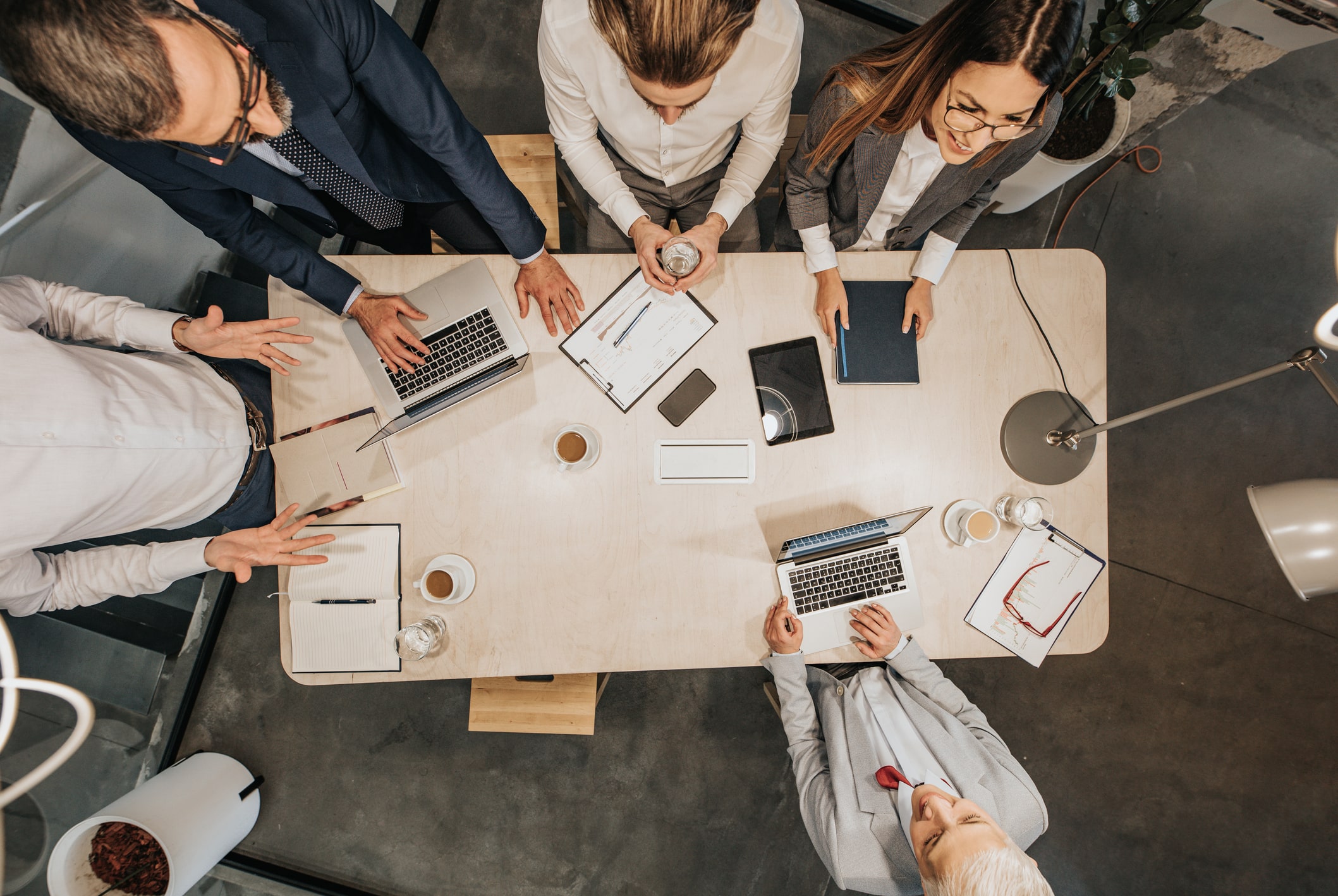 Five people are gathered around a rectangular table, busy with laptops, papers, a coffee cup, notebooks, and a smartphone. The photo is taken from above in a Melbourne Accounting Firm, and the individuals appear to be engaged in a discussion about tax advice in a modern office setting.