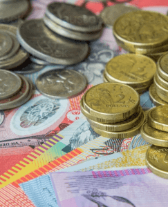 A close-up of a mixture of coins and colorful banknotes, including Australian dollars. The coins and notes are scattered and stacked, showing various denominations. Perfect for business accountants, the background consists of partially visible banknotes with intricate patterns and colors.