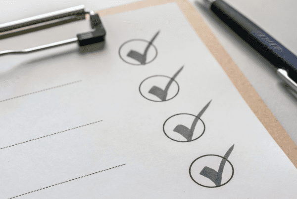 Close-up of a clipboard with a paper displaying a checklist. Three checkboxes are ticked off, indicating completed tasks, with blank lines below. A black pen lies next to the clipboard on a white surface, hinting at the meticulous attention of SMSF Accountants.