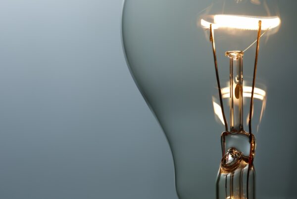 Close-up image of a glowing vintage-style incandescent light bulb, showcasing its filament inside a clear glass bulb against a minimalistic, light blue-gray background—perfectly illuminating the innovative ideas nurtured at Melbourne Accounting Firm.