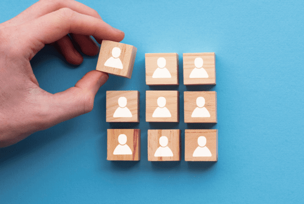 Hand placing wooden block with person icon among others, symbolising team selection and business recruitment strategy.