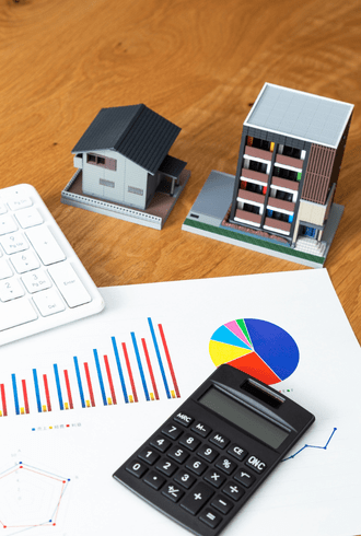 A calculator, keyboard, and financial charts with graphs are on a wooden desk, alongside small model buildings—illustrating how Retail Business Accountants Melbourne support property investment decisions.