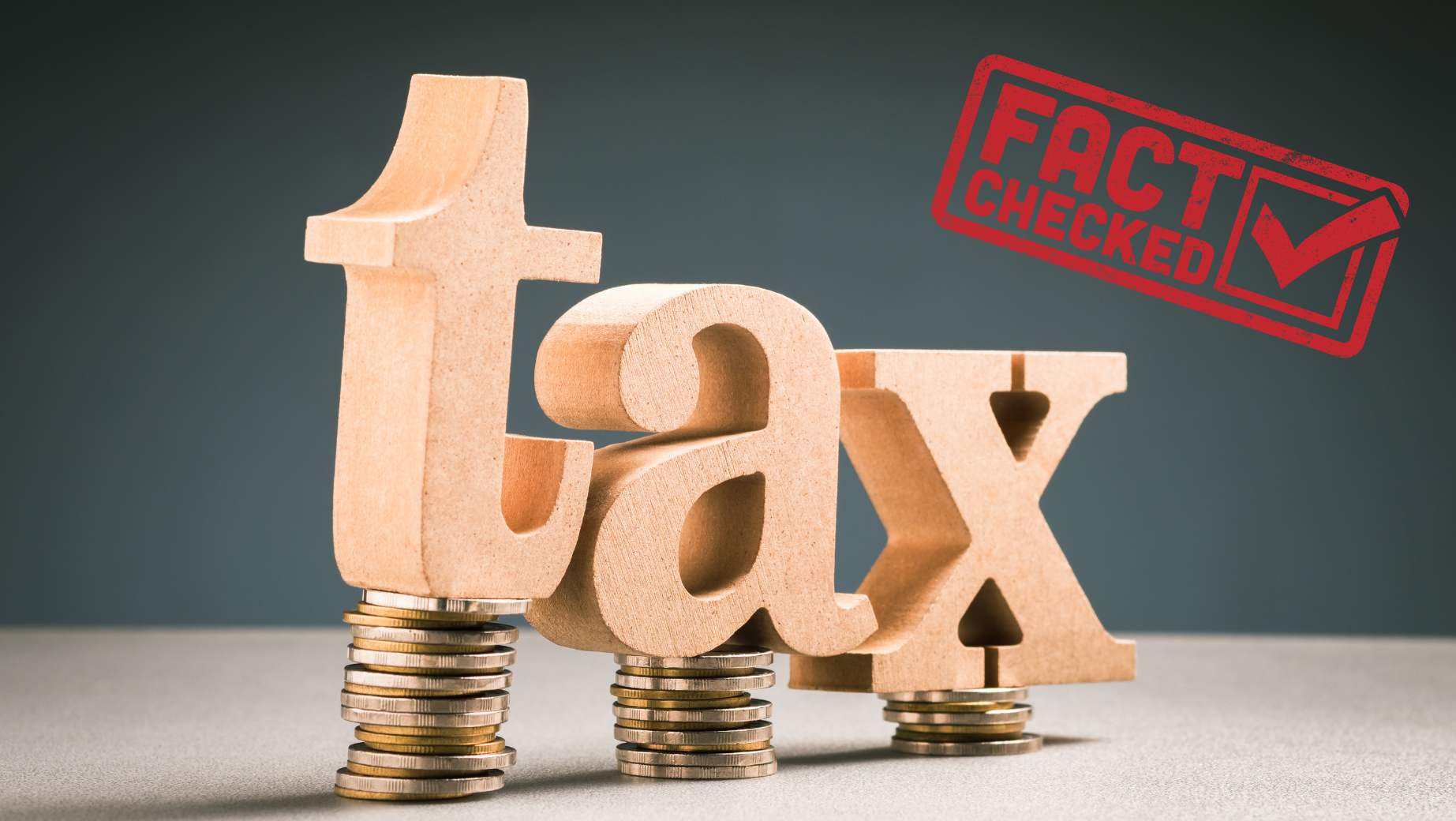 Large wooden letters spelling "tax" are balanced on stacks of coins. To the right, a red stamp with the text "FACT CHECKED" and a checkmark is prominently displayed. The background is dark, providing a stark contrast to the wooden letters and the red stamp, reminiscent of a Melbourne Accounting Firm's office decor.