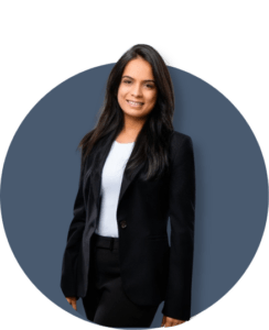 A woman with long dark hair, wearing a black blazer and white top, smiles while standing against a circular blue-gray background.