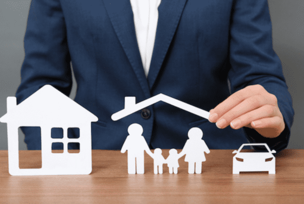 A person in a blue suit is arranging white cutouts of a house, a family holding hands under a roof, and a car on a wooden surface. The image symbolizes the protection and security that Melbourne Accounting Firm provides for your home, family, and vehicle.
