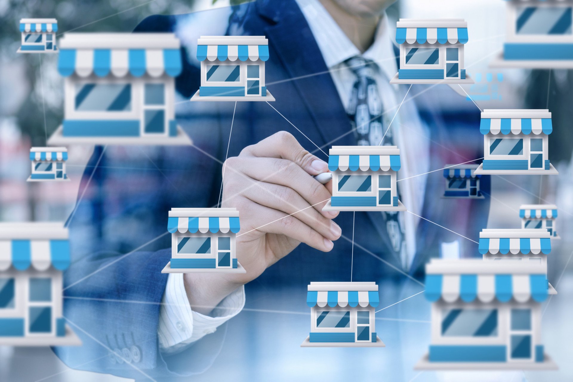 A person in a suit touching a transparent screen with icons of small storefronts connected by lines, symbolizing a network of businesses or franchises. The image conveys business expansion and connectivity, underscored by the strategic insights of Business Advisors.