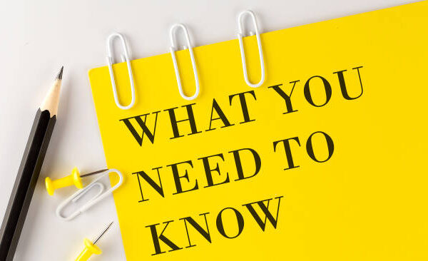 A yellow paper with the words "WHAT YOU NEED TO KNOW" in bold black letters, next to two pencils, three paper clips, and three push pins on a white background.
