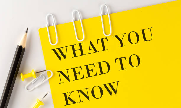 A yellow paper with the words "WHAT YOU NEED TO KNOW" in bold black letters, next to two pencils, three paper clips, and three push pins on a white background.