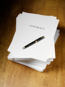 A stack of papers labeled "CONTRACT" sits on a wooden surface with a black and gold pen placed on top of the first page.