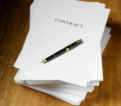 A stack of papers labeled "CONTRACT" sits on a wooden surface with a black and gold pen placed on top of the first page.