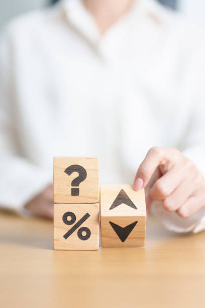 A person in a white shirt stacks wooden blocks with symbols: a question mark, a percent sign, and arrows pointing up and down, suggesting decision-making or financial uncertainty.