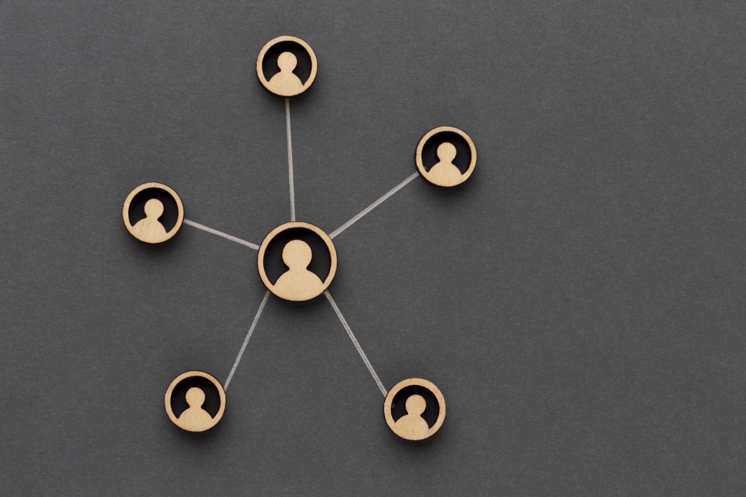 Wooden cutouts of five individuals are connected with strings, forming a network on a dark gray background. One central figure is linked to four surrounding figures, illustrating a hub-and-spoke model of connectivity—an apt metaphor for how our Melbourne Accounting Firm provides expert tax advice through your business accountants.